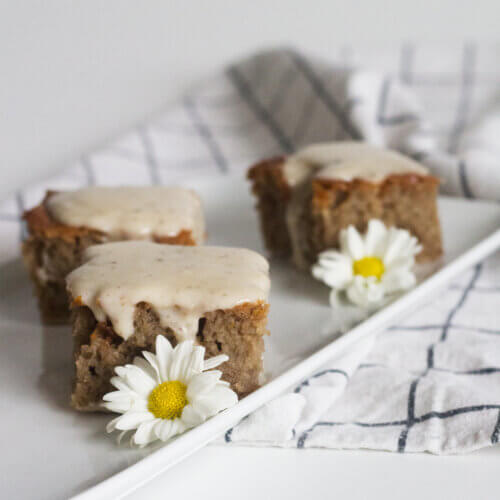 Bolo de mel com calda de coco em uma travessa em pequenos pedaços, decorado com margaridas