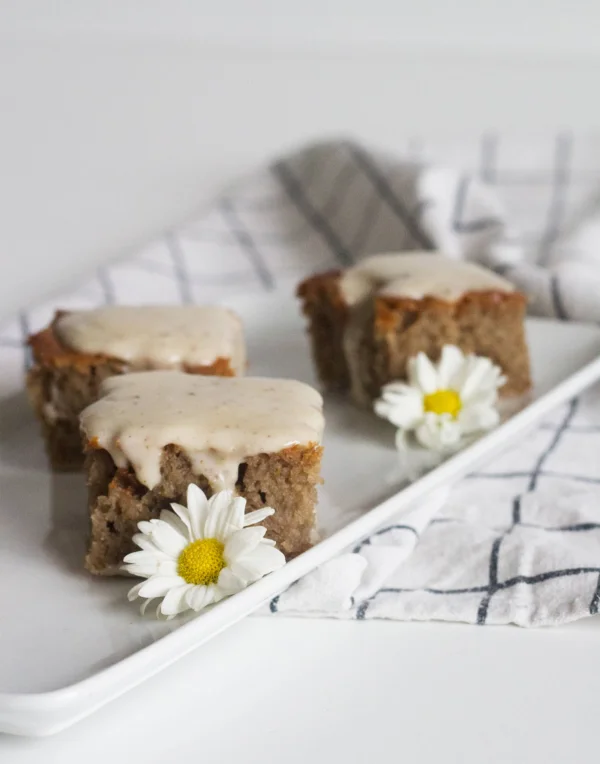 Bolo de mel com calda de coco em uma travessa em pequenos pedaços, decorado com margaridas